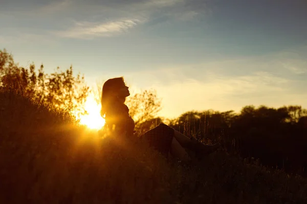 Силуэт молодой женщины, сидящей на холме на закате осенью, концепция человека и природы — стоковое фото