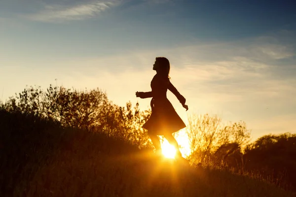 Silueta de una joven mujer ascendiendo en la colina al atardecer, figura chica en el paisaje de otoño —  Fotos de Stock