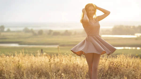 Hermosa chica en un campo en un vestido al atardecer, una mujer joven en una neblina del sol disfrutando de la naturaleza — Foto de Stock