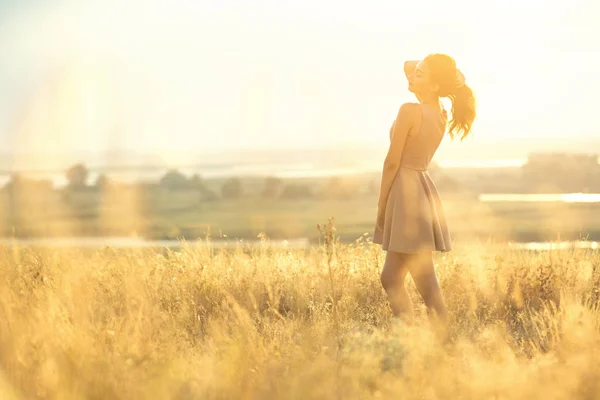 Красивая девушка, гуляющая в поле в платье на закате, молодая женщина, наслаждающаяся летней природой — стоковое фото