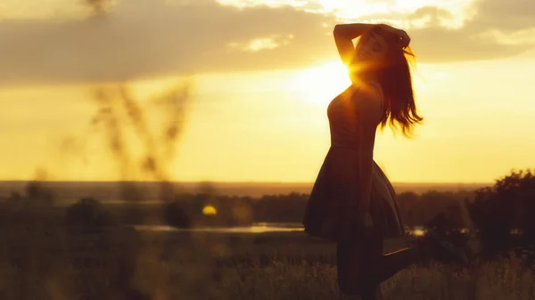 Silhouette of girl in a field at sunset, young woman closed her eyes and enjoying nature — Stock Photo, Image