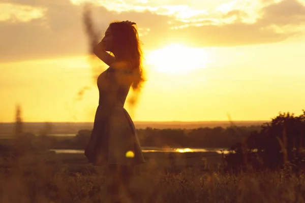 Silueta de una chica de ensueño en un campo al atardecer, una joven disfrutando de la naturaleza — Foto de Stock