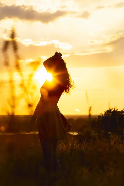 Silueta de una hermosa chica en un vestido al atardecer en un campo, figura de mujer joven disfrutando de la naturaleza, concepto de ocio —  Fotos de Stock