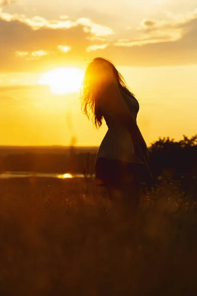 Silhouette of a beautiful girl in a dress at sunset in a field, figure of young woman enjoying nature, concept of leisure — Stock Photo, Image