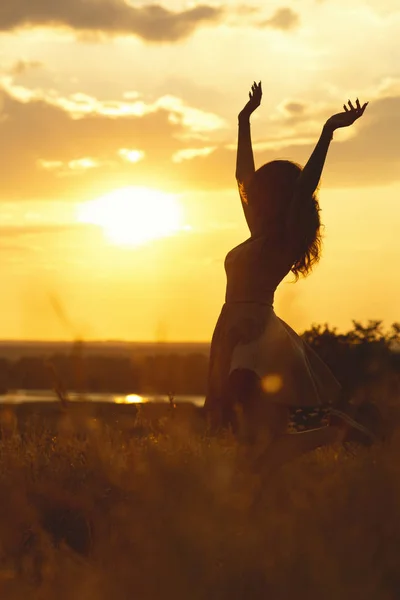 Silhouette eines schönen Mädchens, das in einem Kleid bei Sonnenuntergang auf einem Feld tanzt und sich dreht, eine glückliche junge Frau, die die Natur genießt — Stockfoto