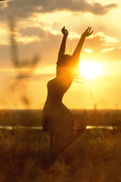 Silhouette eines schönen Mädchens, das in einem Kleid bei Sonnenuntergang auf einem Feld tanzt und sich dreht, eine glückliche junge Frau, die die Natur genießt — Stockfoto