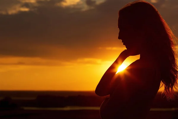 Sziluettje egy gyönyörű romantikus lány naplementekor, arc profilja a fiatal nő, hosszú hajú, meleg időjárás — Stock Fotó