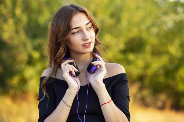 Porträtt av en vacker flicka med hörlurar, ung kvinna lyssnar på musik på naturen i fält — Stockfoto