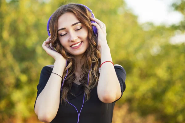 Lycklig tjej med hörlurar på huvudet, ung kvinna lyssnar på musik på naturen i fältet — Stockfoto