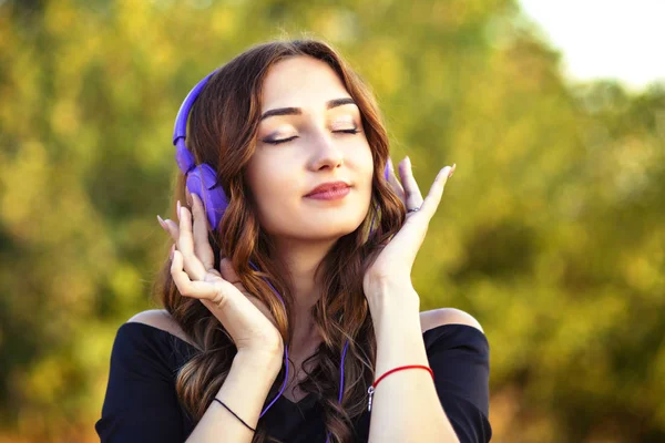 Porträtt av en vacker tonåring flicka med hörlurar på huvudet, ung kvinna lyssnar på musik på naturen — Stockfoto