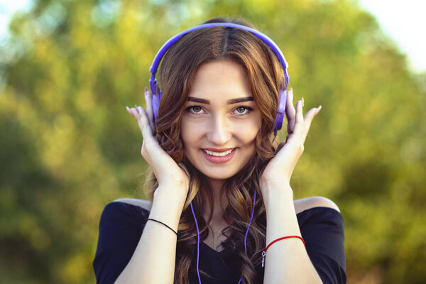 portrait of a beautiful happy teenager girl with headphones on head, young woman listening to music on the nature