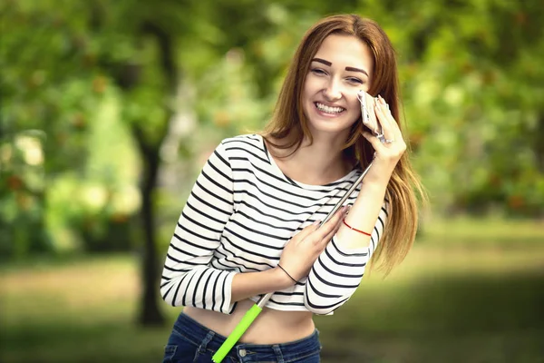 Porträtt av en skrattande flicka i en stadspark med smartphone på Selfie Stick — Stockfoto