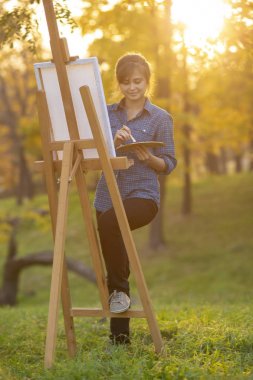 Kadın sanatçı doğadaki sehpaya resim çiziyor, fırçası ve paleti olan bir kız, yaratıcılık ve hobi kavramı