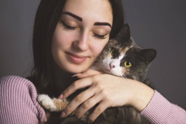 bir kızın portresi yavaşça kedi yanağını bastırdı, gözleri kapalı kız gri bir arka plan üzerinde kedi kucaklıyor, kavram evcil hayvan