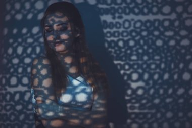 bir pencere perdesinden mavi ışık desenli boynunun arkasında bir el ile güzel bir şehvetli kız portresi