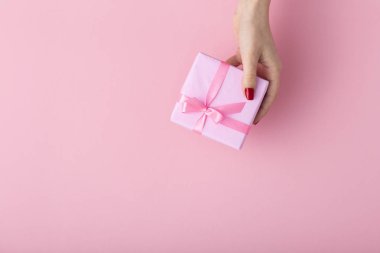 elinde bir hediye tutan kız, kadın elleri bir pastel pembe arka plan üzerinde dekoratif kağıt sarılı kutuyu açmak, üst görünümü, konsept tatil ve hediyeler