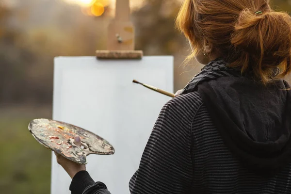 Doğadaki genç kadın sanatçı, doğadaki bir sehpanın üzerine resim çiziyor. — Stok fotoğraf