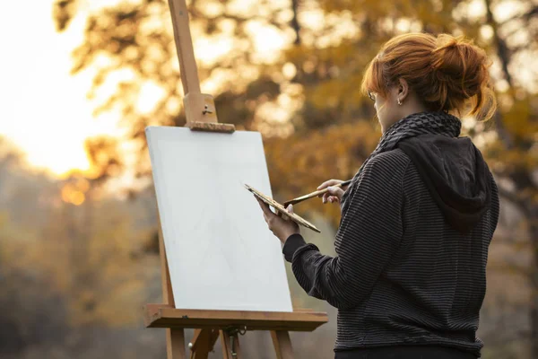 Dziewczyna rysunek obraz na sztalara w przyrodzie, młoda kobieta z pędzlem farby wśród jesiennych drzew, pojęcie kreatywności i hobby — Zdjęcie stockowe
