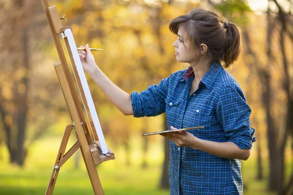 Kadın sanatçı doğadaki sehpaya resim çiziyor, fırçası ve paleti olan bir kız, yaratıcılık ve hobi kavramı — Stok fotoğraf