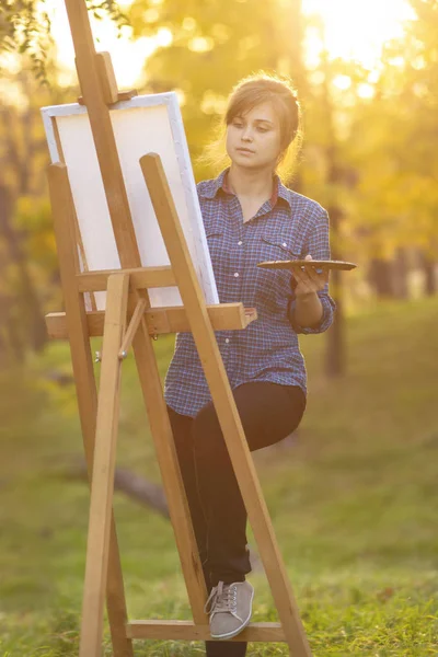 woman artist drawing a picture on an easel in nature, a girl with a brush and a palette, a concept of creativity and a hobby