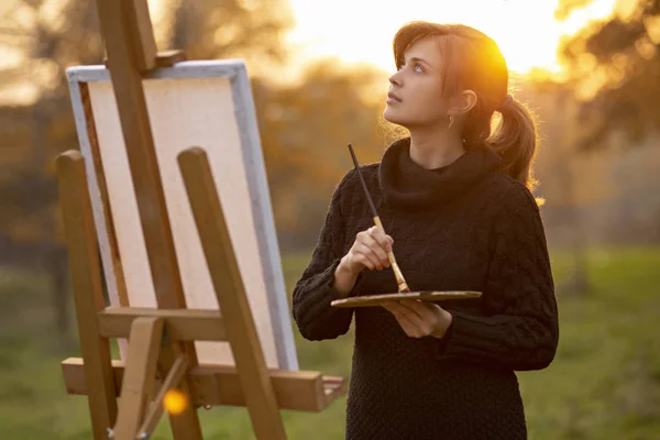 Fiatal nő művész rajz egy festőállványt a természet naplementekor ősszel, koncepció a kreativitás és a hobbi — Stock Fotó