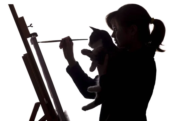 Silhouette de femme peignant un tableau sur chevalet, un profil d'une fille tenant pinceau et chat dans les mains, concept art et animaux de compagnie — Photo