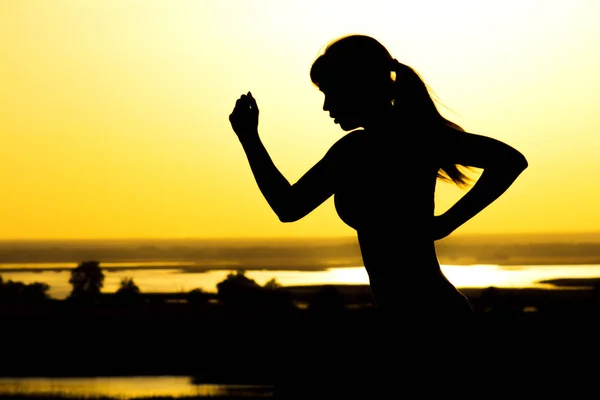 Silhueta de uma mulher correndo sobre a natureza ao pôr do sol, esportes perfil feminino, conceito de esporte, lazer e cuidados de saúde — Fotografia de Stock