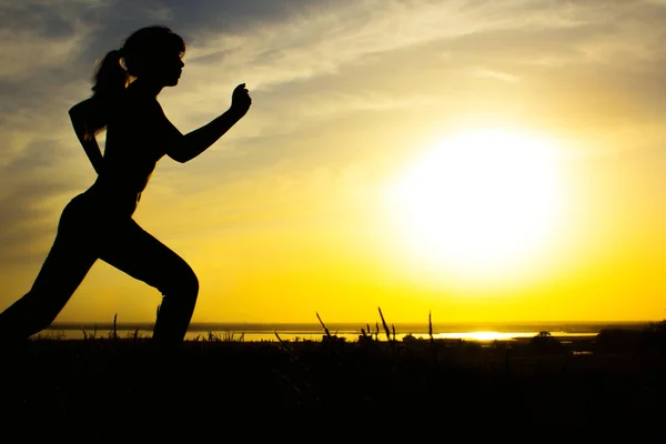 Silhouette di una donna che fa jogging sulla natura al tramonto, profilo sportivo femminile, concetto di sport, tempo libero e salute — Foto Stock