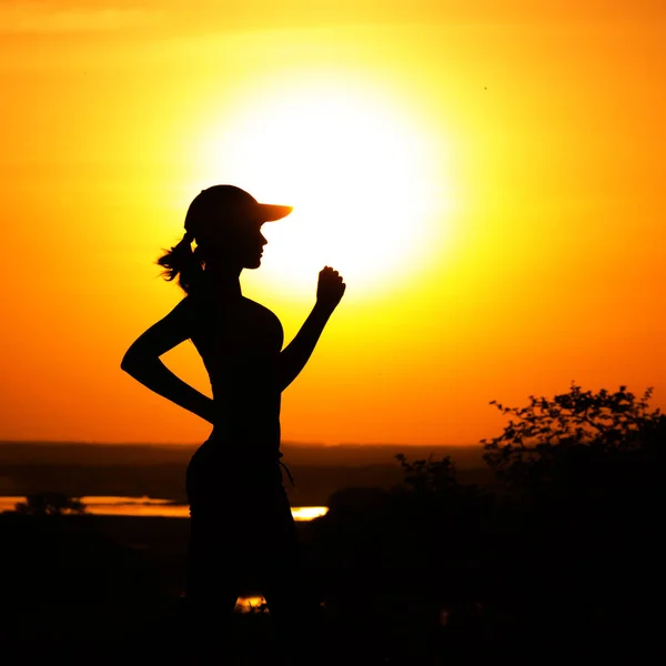 Silhouette di una donna che fa jogging sulla natura al tramonto, profilo sportivo femminile, concetto di sport e tempo libero femminile — Foto Stock