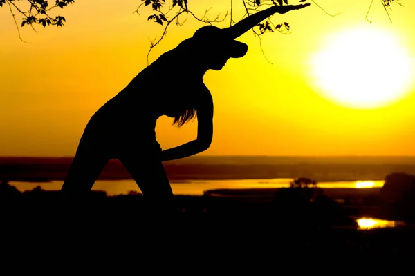 Silhouette of a young woman engaged in fitness in nature at sunset, a sports female profile, the concept of sport and healhcare — Stock Photo, Image