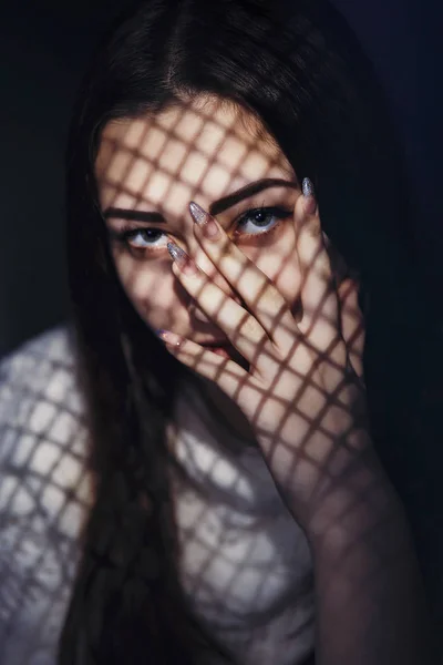 beautiful girl with a light pattern on the face in the form of a grid, a portrait of a young woman with a secret covering his face with his hand, the concept of female beauty