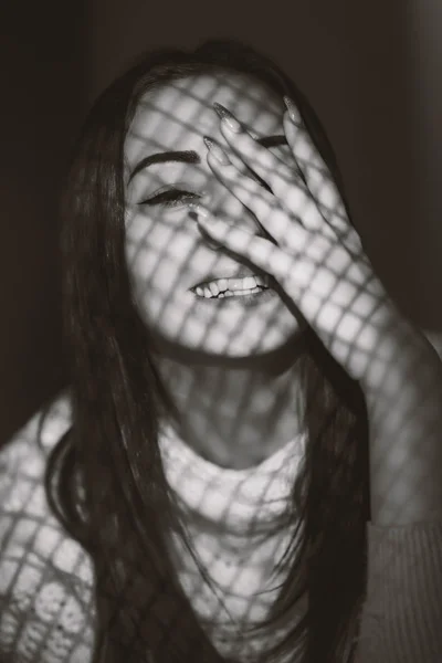 Menina com um padrão de luz no rosto na forma de uma grade, um retrato de uma jovem mulher sinceramente rindo, o conceito de beleza feminina e emoções — Fotografia de Stock