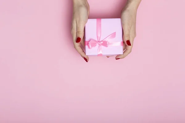 Menina segurando um presente em mãos, as mulheres dando uma caixa de presente envolto em papel decorativo em um fundo rosa pastel, vista superior, férias conceito — Fotografia de Stock