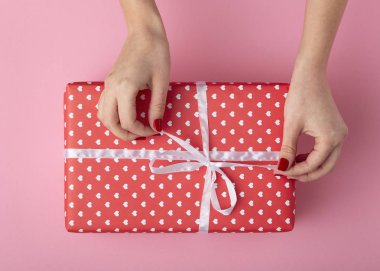 elinde bir hediye tutan kız, kadın elleri bir pastel renkli pembe arka plan üzerinde dekoratif kağıt sarılı kutuyu açmak, üst görünümü, konsept tatil ve hediyeler