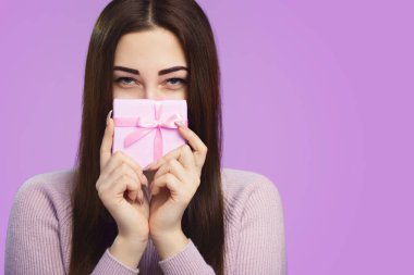 kız bir hediye kutusu ile ağzını kapatır, yarım kapalı yüzü ve daraltılmış gözleri ile bir kadın gizemli bir görünüm ile çerçeve içine bakar, tatil ve duygu kavramı