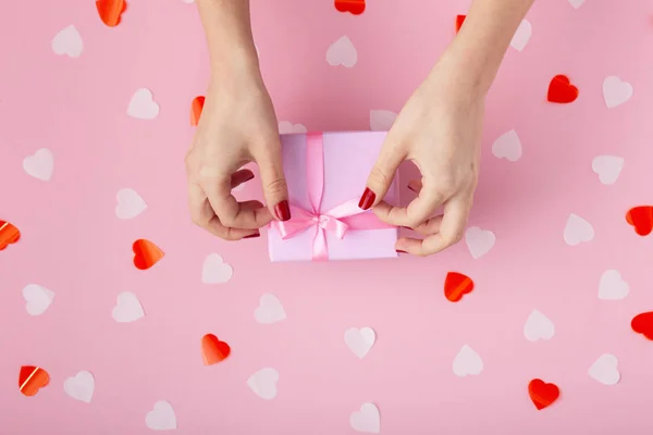 Vrouwelijke handen met een geschenk doos op een Pastel gekleurde achtergrond top uitzicht, het meisje het openen van een geschenk en ontkoppelen van een lint Bow, het concept van de feestdagen — Stockfoto
