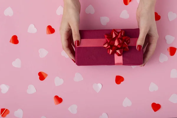 Vrouwelijke handen met een geschenk doos op een Pastel gekleurde achtergrond top uitzicht, het meisje met een cadeautje met decoraties, het concept van vakantie en liefde — Stockfoto