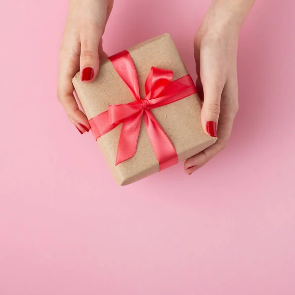 Menina segurando um presente em mãos, mulheres com caixa de presente em mãos envolvidas em papel decorativo sobre fundo rosa, vista superior, conceito de férias e presentes — Fotografia de Stock