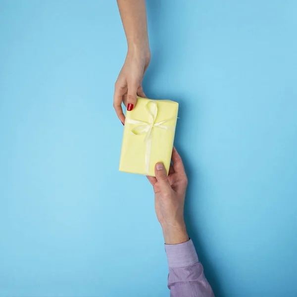 Hombre le da a una chica un regalo de mano a mano, caja envuelta en papel decorativo con un fondo de lazo, el concepto de vacaciones, el amor y las relaciones, vista superior — Foto de Stock