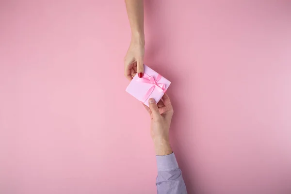 Homem dá uma menina um presente de mão em mão, caixa envolta em papel decorativo em um fundo pastel rosa, o conceito de feriados, vista superior — Fotografia de Stock