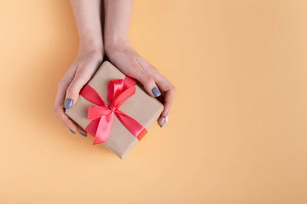Niña sosteniendo un regalo en las manos, las mujeres con caja de regalo en las manos envueltas en papel decorativo sobre un fondo de color pastel, vista superior, concepto de vacaciones — Foto de Stock