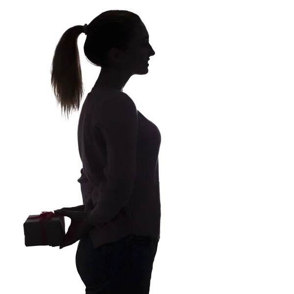 Silhouette di una giovane donna con un regalo alle sue spalle, una ragazza con una scatola con un fiocco fa una sorpresa? concetto di vacanze — Foto Stock