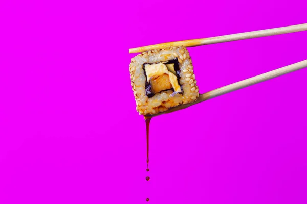 succulent roll between chopsticks on a colored background, drops of soy sauce dripping from sushi, food background, Japanese cuisine