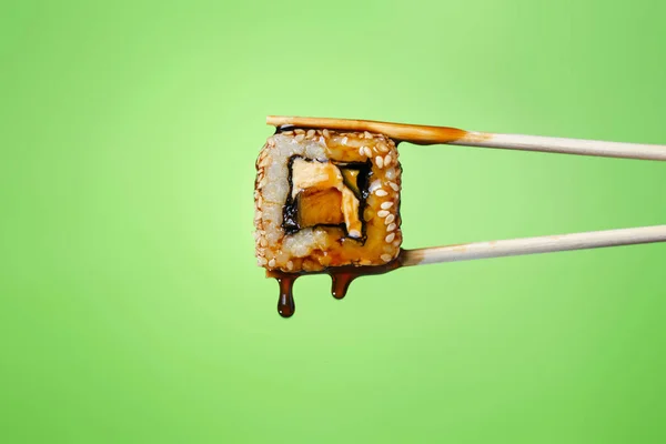succulent roll between chopsticks on a colored background, drops of soy sauce dripping from sushi, food background, Japanese cuisine