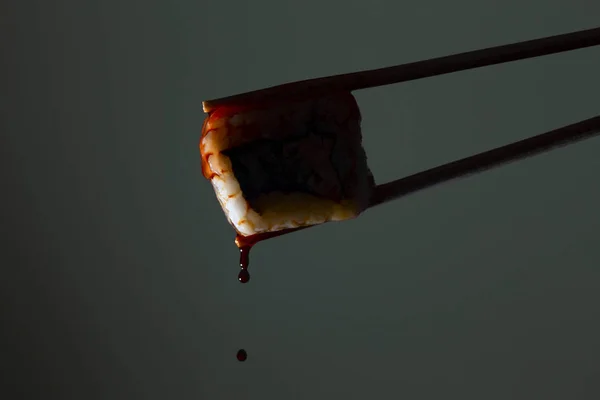 silhouette of succulent roll between chopsticks on a colored background, drops of soy sauce dripping from sushi, food background, Japanese cuisine