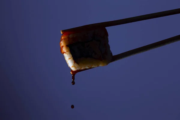Silueta šťavnaté ropoty mezi hůlky na barevném pozadí, kapky sójové omáčky kapající z sushi, potravinové pozadí, japonská kuchyně — Stock fotografie