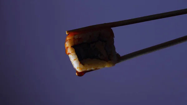silhouette of succulent roll between chopsticks on a colored background, drops of soy sauce dripping from sushi, food background, Japanese cuisine