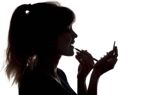 Silueta de la mujer haciendo maquillaje delante del espejo de bolsillo en las manos sobre fondo blanco aislado —  Fotos de Stock