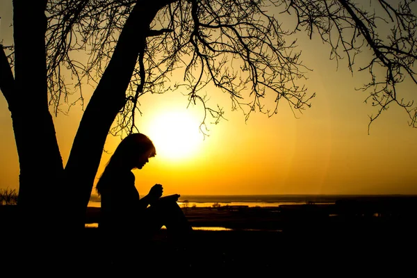 Silhueta de mulher orando a Deus na natureza witth a Bíblia ao pôr do sol, o conceito de religião e espiritualidade — Fotografia de Stock
