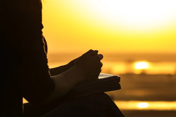 Silhouette des mains de la femme priant Dieu dans la nature witth la Bible au coucher du soleil, le concept de religion et de spiritualité — Photo